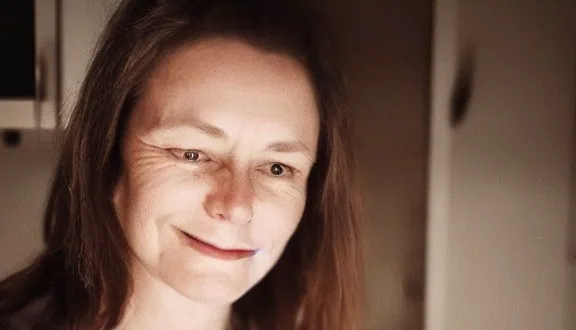 Visage souriant d'une femme dans une lumière chaude et tamisée, sans téléphone.