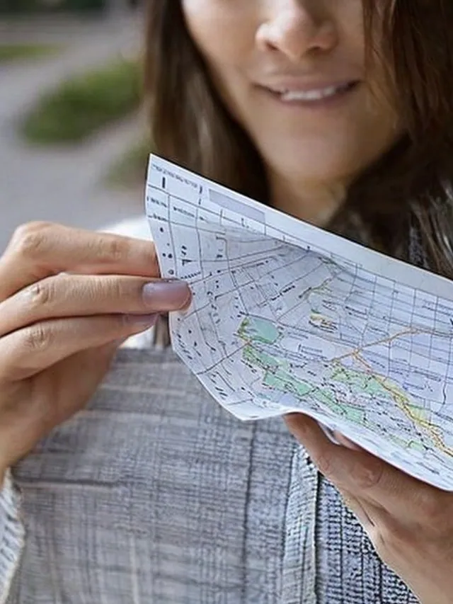 Gros plan sur des mains qui tiennent une carte routière, bas du visage souriant.