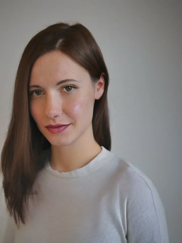 Portrait d'une femme aux cheveux bruns lisses, pull clair, fond gris.