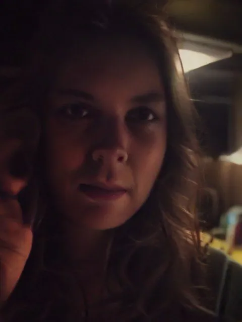 Visage de femme dans la pénombre, une main près de la joue, sans téléphone visible.